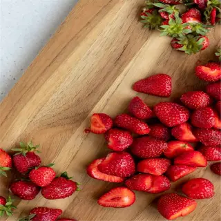 fresh strawberries, some whole and some sliced, on a wooden cutting board with a knife