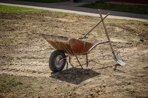 garden wheelbarrow debris with shovels leaning against it on dirt ground