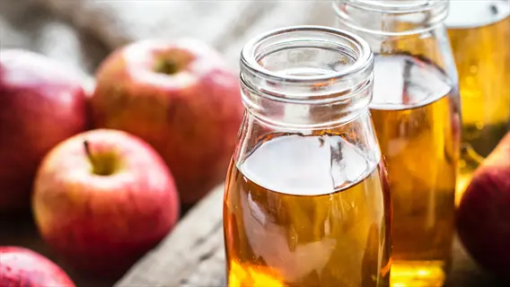 glass bottles of apple cider vinegar with fresh apples on a rustic wooden surface