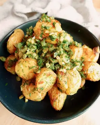 golden roasted dill potato salad with fresh herb topping on a dark plate