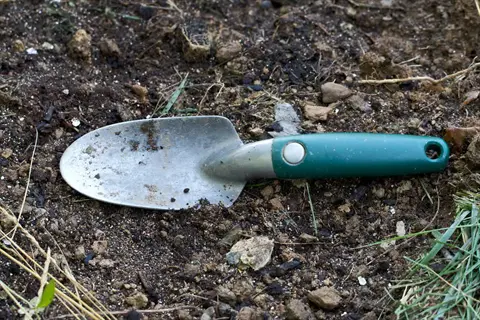 green-handled garden hand trowel resting on dark soil with grass and debris in a garden setting