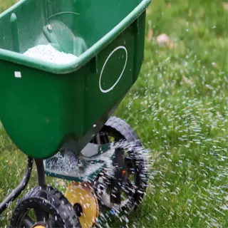 green lawn fertilizer spreader in action, spreading granules on grass