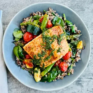 grilled salmon on a parsley asparagus bed with wild rice, roasted cherry tomatoes, zucchini, and leafy greens, garnished with fresh herbs
