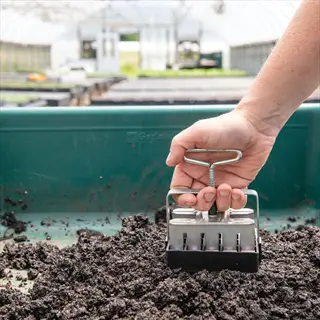 hand pressing soil blocker tool to form compressed soil blocks in a greenhouse nursery tray