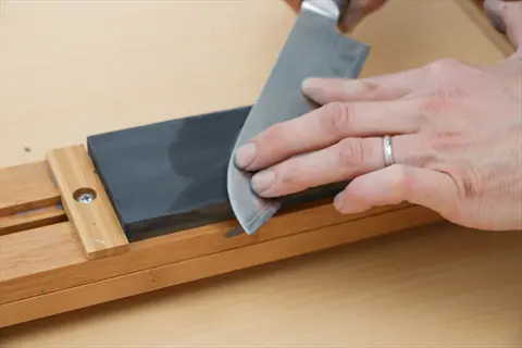 hands using a tool sharpening stone to sharpen a chef's knife on a wooden guide
