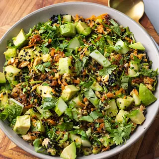 herb garnished salad bowl with avocado, shredded carrots, cucumber, black sesame seeds, and fresh cilantro for culinary presentation