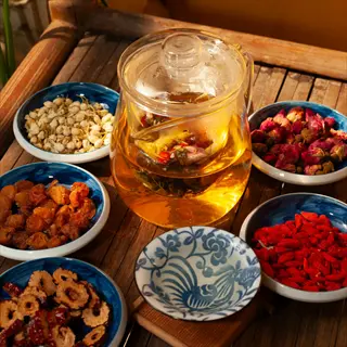 herbal tea preparation with glass teapot and assorted dried herbs in blue-and-white bowls on a wooden table