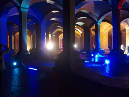 historic brick underground water tank interior illuminated by blue and purple stage lighting, featuring arched ceilings, columns, and people at a cultural event