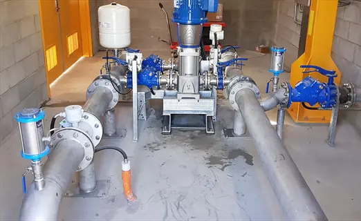 industrial rainwater filtration system: blue valves, stainless steel pipes, pressure gauges, and pump infrastructure in concrete utility room