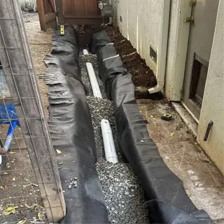 installed drainage solutions with pipes and gravel, covered by black fabric