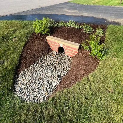 landscape featuring a brick culvert over gravel channel surrounded by raised mulch beds with plants - a raised bed drainage solution for runoff management