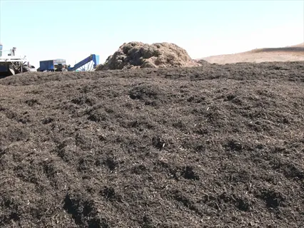 large municipal compost pile in an outdoor facility, with additional green waste compost mounds and heavy machinery visible in the background