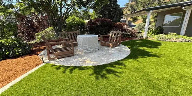 lush backyard with circular stone patio, wooden furniture, and prominent compact mondo grass border framing landscaped areas