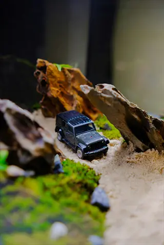 miniature diorama with toy jeep driving through sandy path surrounded by miniature mondo grass and rock formations
