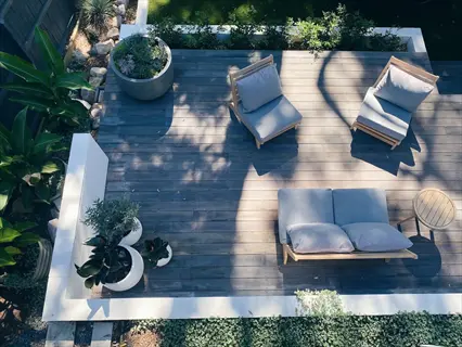 modern shaded patio with wooden deck, outdoor seating, and lush potted plants including tropicals and ground cover under dappled sunlight