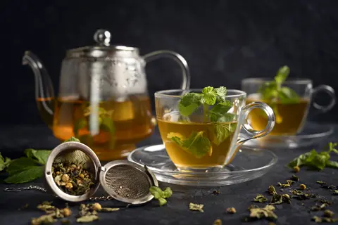 moroccan mint tea served in glass teapot and cups with fresh mint sprigs and tea infuser on dark surface