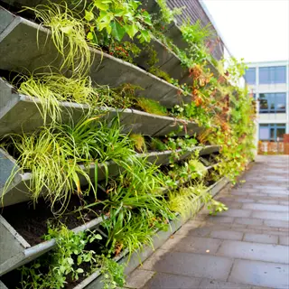 multi-tiered vertical garden with integrated drip irrigation containers growing lush greenery along an urban sidewalk