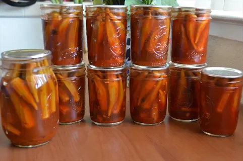 multiple glass jars of pickled okra with reddish brine arranged on a wooden surface