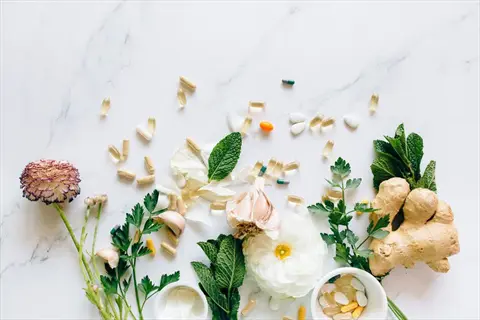 natural medicine cabinet arrangement with fresh herbs, ginger, garlic, ranunculus flower, and medicinal supplements on marble surface