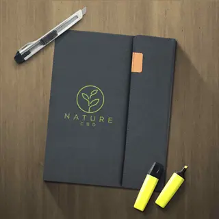 nature-themed garden journal notebook with 'nature cbd' text and leaf logo, surrounded by a pen, utility knife, and yellow highlighters on a wooden surface