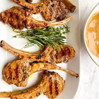 oregano lamb seasoning on grilled lamb chops with rosemary-thyme garnish, served on a white platter with a side of sauce