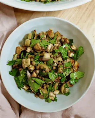 oregano roasted vegetables in a bowl: chunky roasted veggies mixed with fresh parsley and lentils, served in a light gray bowl on a wooden surface with a pink cloth