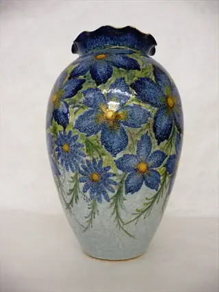 ornate glazed ceramic pot with blue floral patterns, ruffled rim, and artist signature
