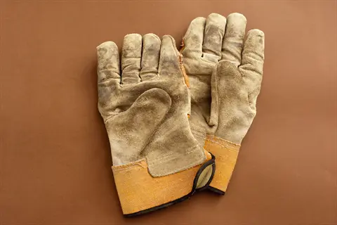 pair of worn leather gardening gloves with orange cuffs on brown background