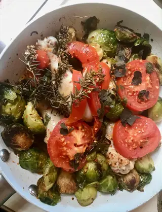 pan of sautéed brussels sprouts with chicken, tomatoes, herbs, and spices, garnished with fresh rosemary