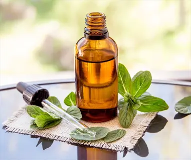 peppermint essential oil in amber glass bottle with dropper, surrounded by fresh peppermint leaves on burlap cloth