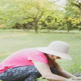 person in a hat tending to plants in a garden
