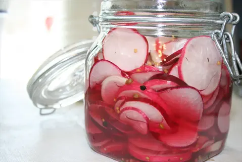 pickled radishes in a glass jar container with vibrant red-and-white slices and spices in brine