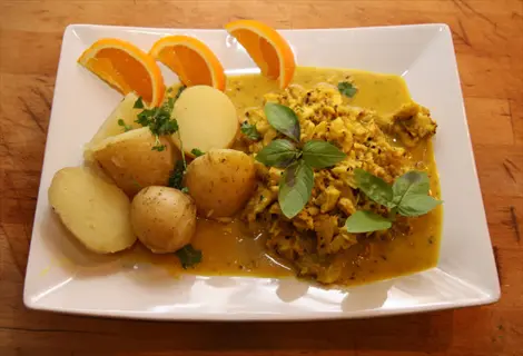 plate of lemongrass seafood curry with boiled potatoes and orange slices, garnished with fresh herbs