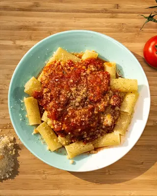 plate of rigatoni pasta with homemade tomato sauce, grated cheese, and fresh tomatoes on a wooden table