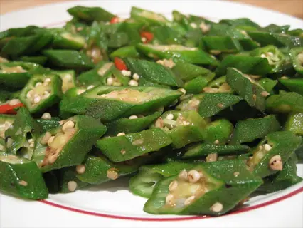 plate of wok-fried okra slices with visible seeds and red chili flakes, served on a white plate with red rim