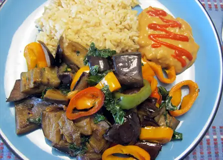 plate with eggplant stir fry featuring bell peppers, served with brown rice and swirled sauce