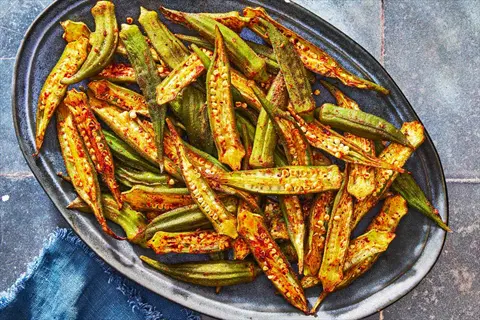 platter of oven roasted okra halves with spicy seasoning, arranged on a blue-rimmed plate against a tiled background