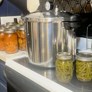 pressure canning setup with canned green beans jars on a kitchen stove, alongside a pressure cooker and other canned food jars