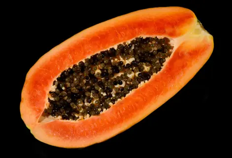 ripe pawpaw fruit halved lengthwise, revealing orange flesh and glossy black seeds