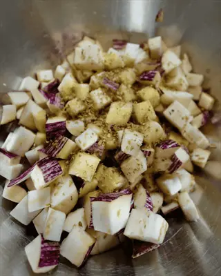 roasted eggplant cubes preparation: raw diced eggplant with herbs and oil in a metal bowl, showing the roasting technique's prep step