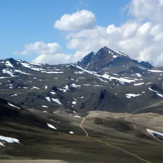 scenic view of alpine zones with snow-patched mountains and a gravel road