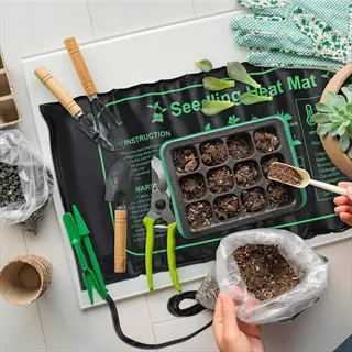 seedling heat mat labeled with instructions, surrounded by gardening tools, seed tray, gloves, and a hand in a home gardening setup