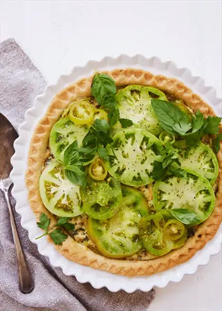 sliced green tomato pie with fresh basil and parsley in white fluted dish, served with vintage spoon on cloth napkin