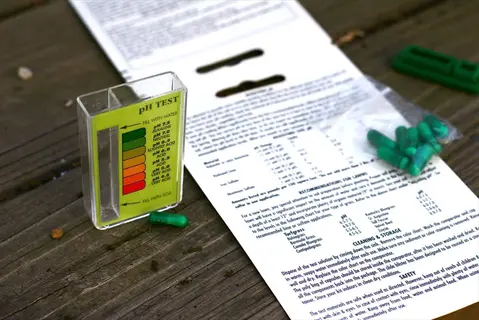soil ph testing kit with color-coded indicator panel (green to red gradient), instructional sheet, and green capsules on weathered wooden surface