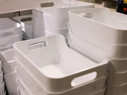 stacks of white plastic storage bins with cutout handles in a retail warehouse. the uniform containers are neatly stacked, showcasing their practical design for organization and storage solutions