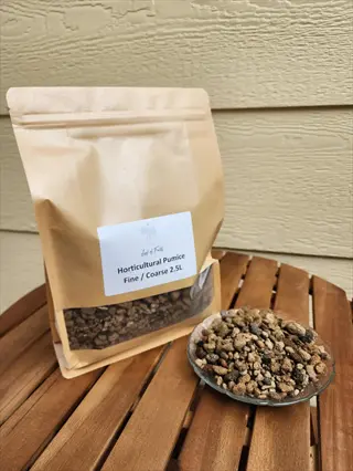 standing bag labeled 'horticultural pumice fine/coarse 2.5l' and a small glass dish filled with the porous, lightweight rocks. both sit on a wooden table against a wooden siding background