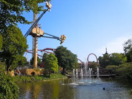 sunny amusement park lake featuring vertigo fountain with towering rides in the background
