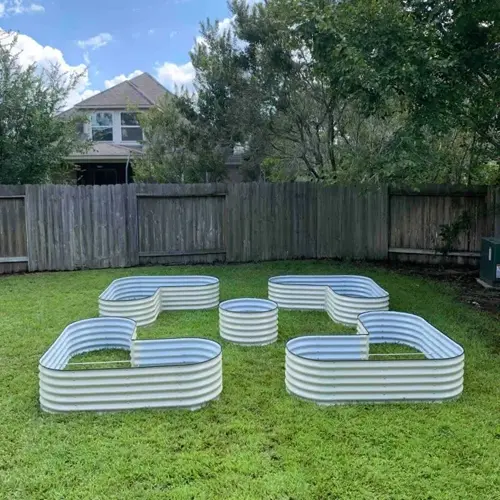 symmetrical arrangement of four curved corrugated metal raised garden bed materials on lush green grass in a fenced backyard with residential houses in the background
