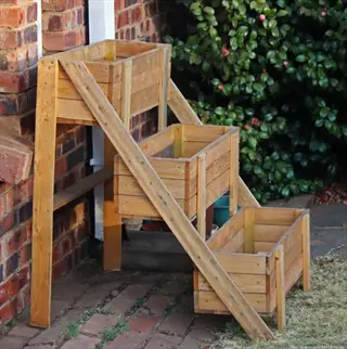 three-tiered wooden herb planter against brick wall in garden courtyard