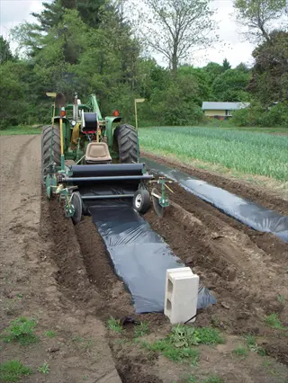 tractor installing plastic mulch on agricultural garden beds - plastic garden bed drainage solution for soil moisture management and plastic bed optimization in farming